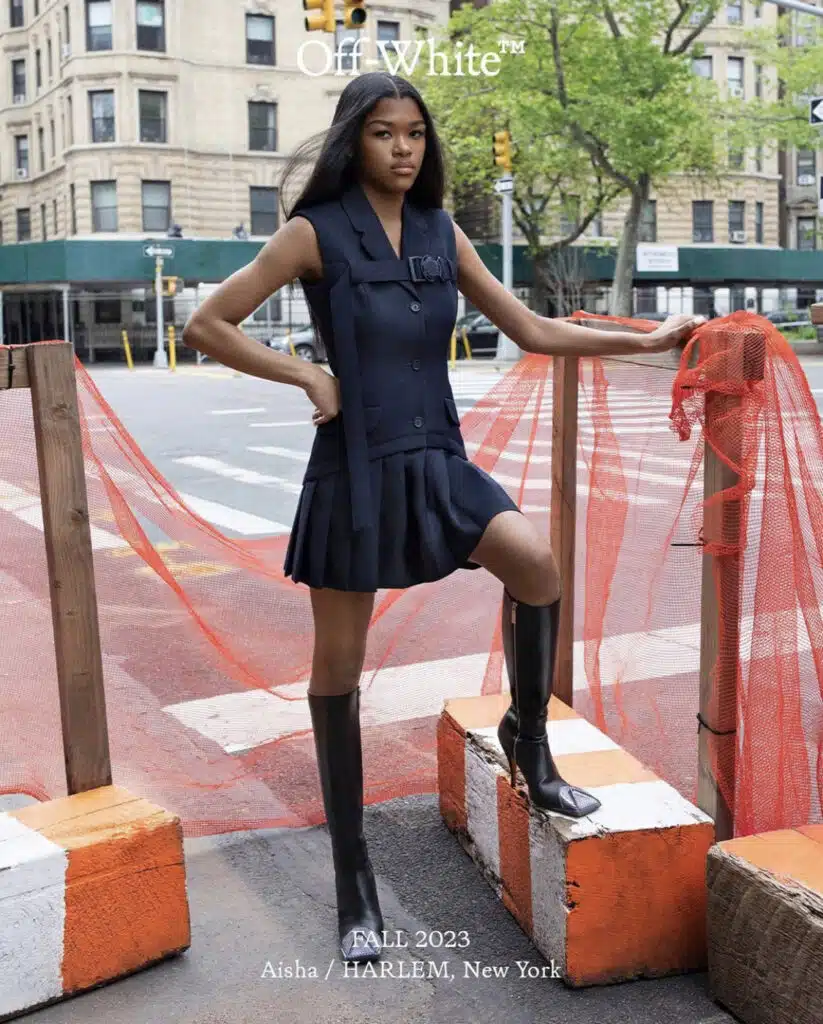 A woman in black dress and boots standing on the side of road.