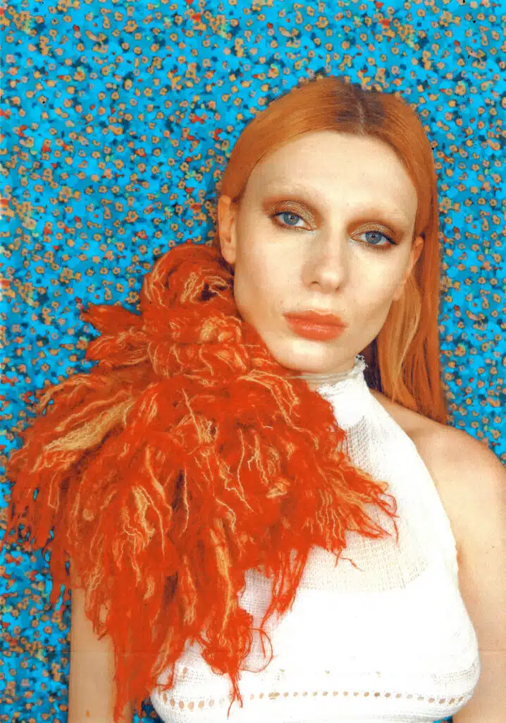 A woman with red hair and an orange feather in her shoulder.