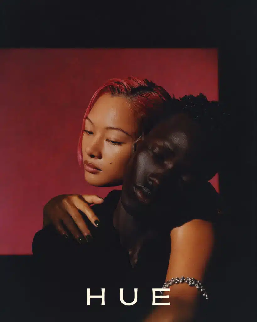 A woman hugging another person in front of a red wall.