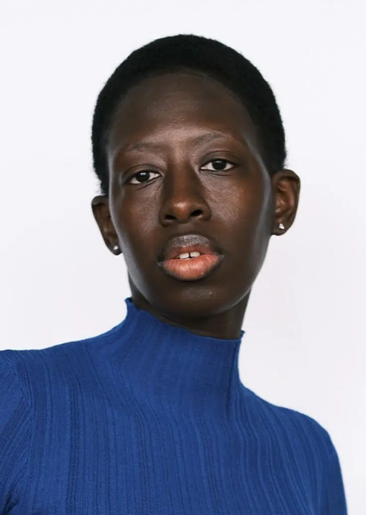 A man with dark skin wearing a blue sweater.