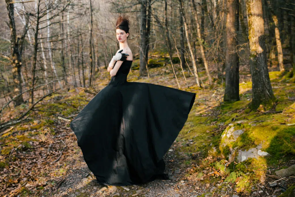 A woman in black dress standing on the side of a forest.