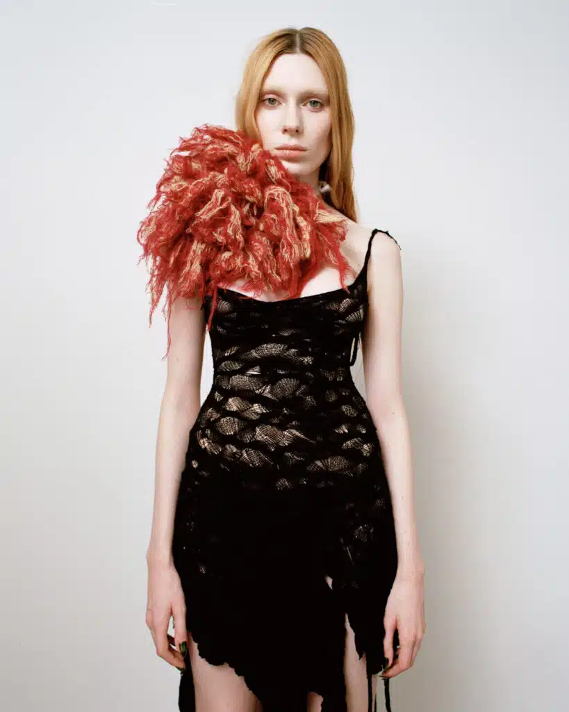 A woman in black dress holding up a red feather.