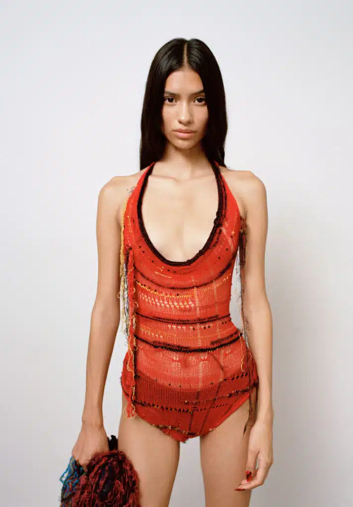 A woman in a red bathing suit standing up against a wall.