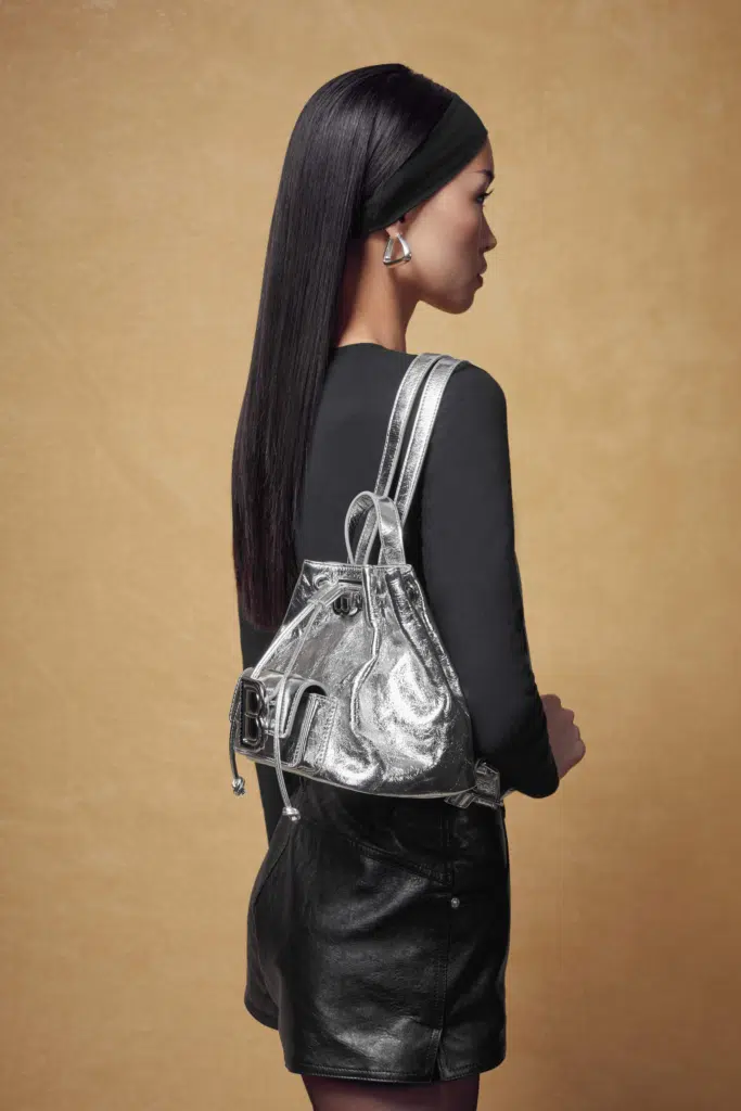 A woman with long hair and black dress holding a silver bag.