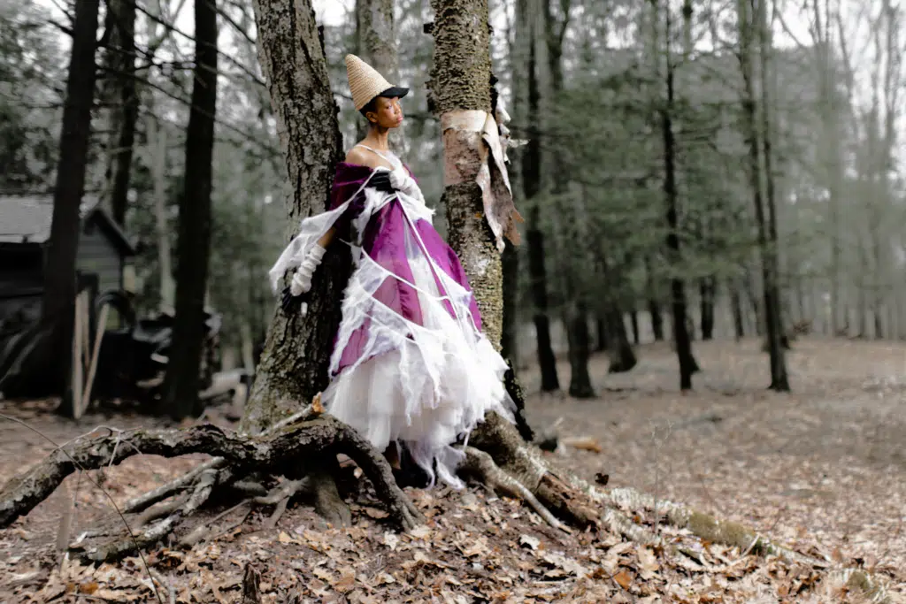 A woman in purple dress standing next to tree.