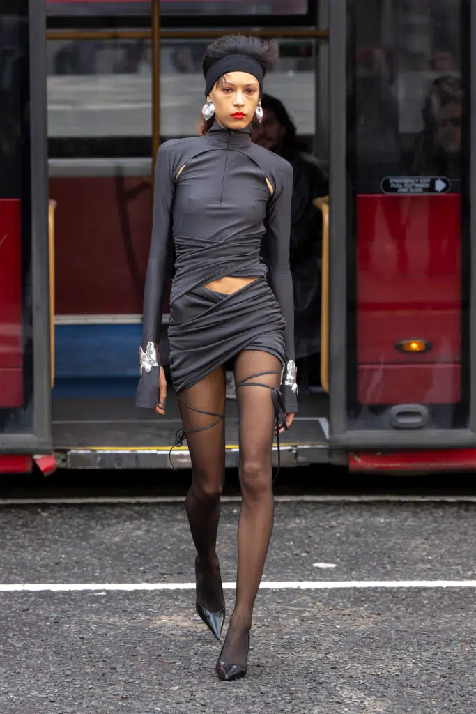 A woman in black dress and stockings walking on the street.