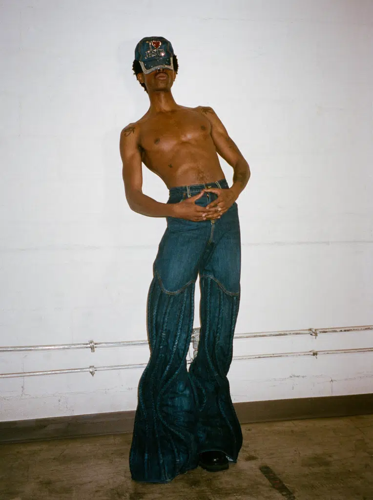 A man in blue pants and a mask standing next to a wall.