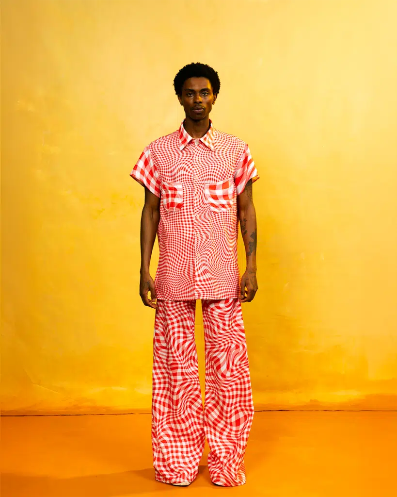 A man in pink and white shirt standing next to wall.