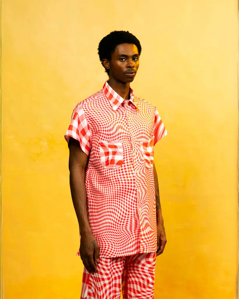 A man in red and white shirt standing next to yellow wall.