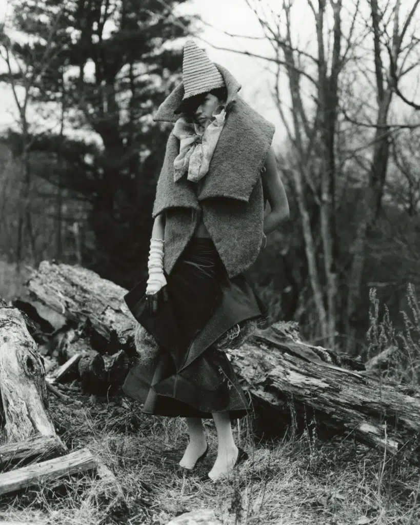 A woman in an old fashion outfit standing next to a tree.