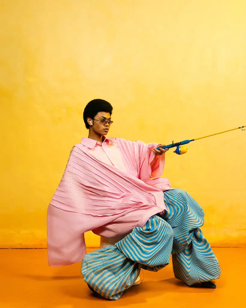 A man in pink shirt and blue pants holding a pair of scissors.