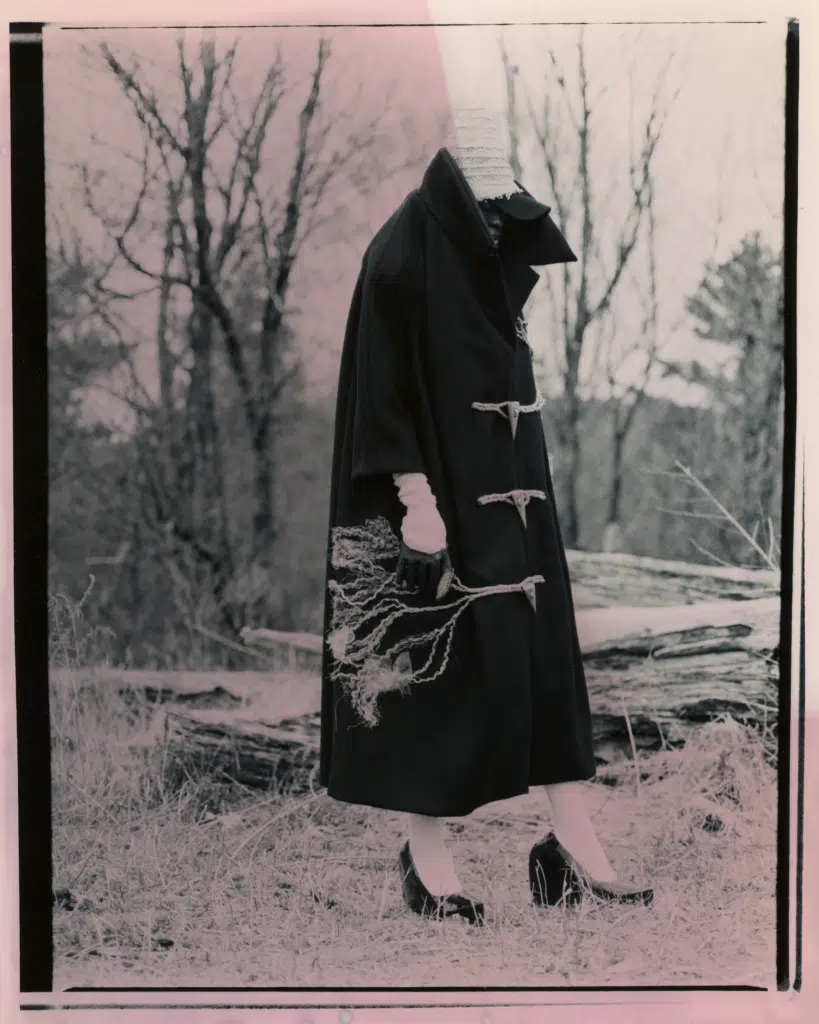 A woman in black coat and white shoes holding a bag.