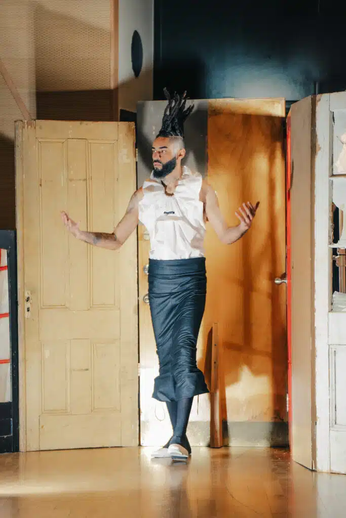 A man in a white shirt and black skirt standing next to two doors.