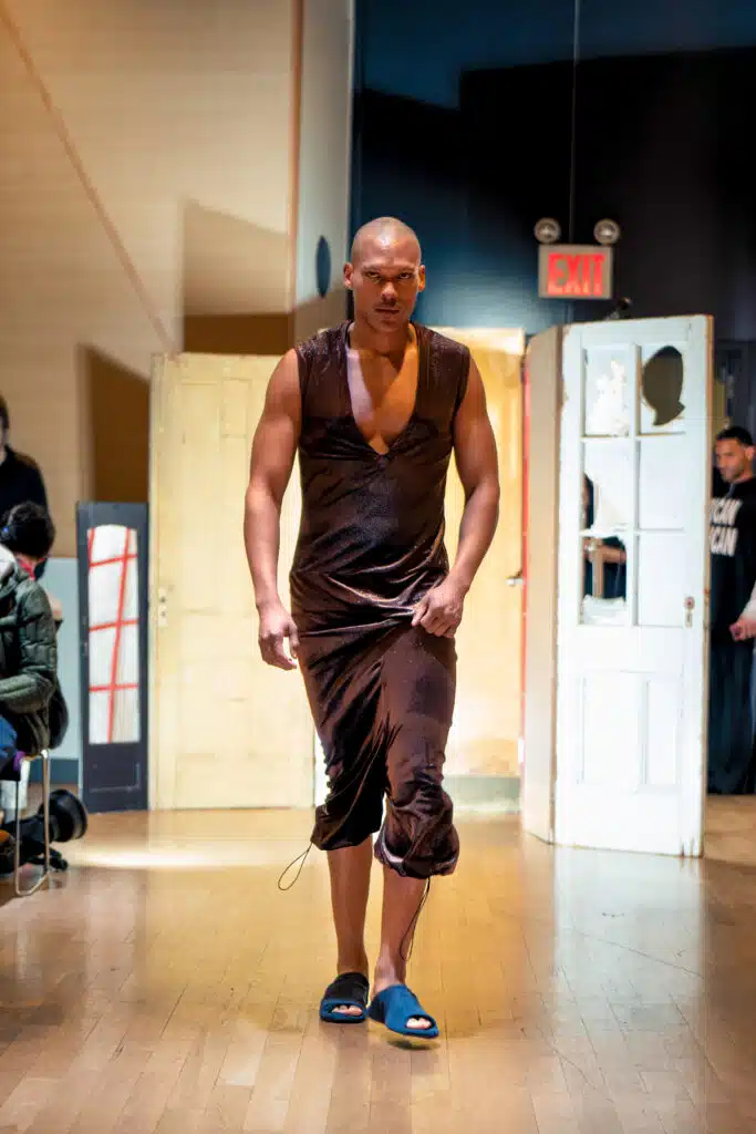 A man in brown shirt and shorts walking on wooden floor.