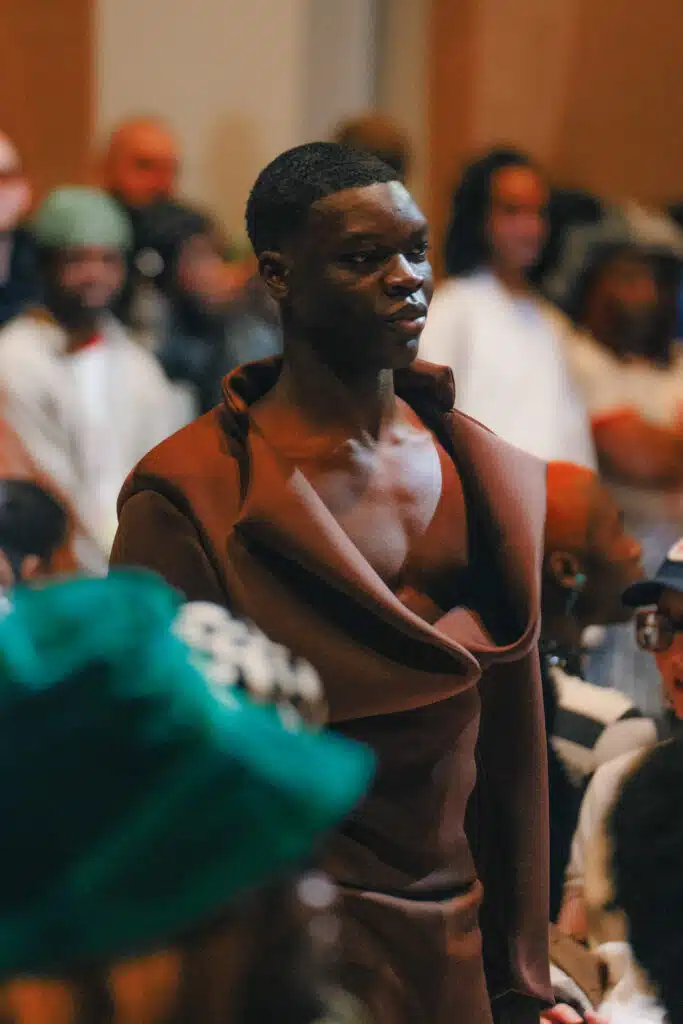 A man in brown shirt and green bag standing next to crowd.