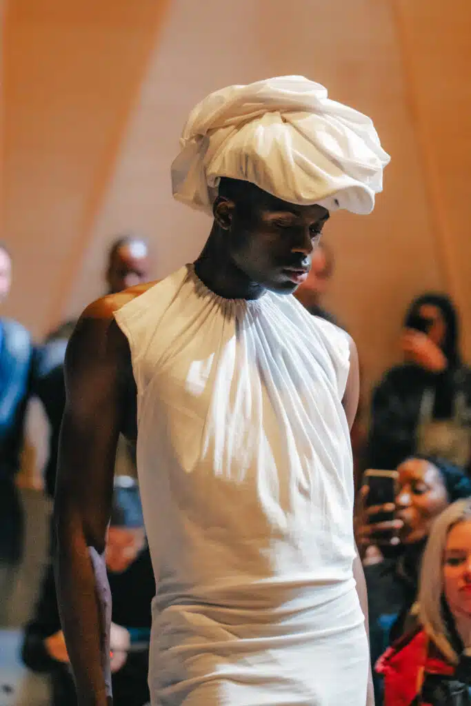 A man in white shirt and hat standing next to crowd.