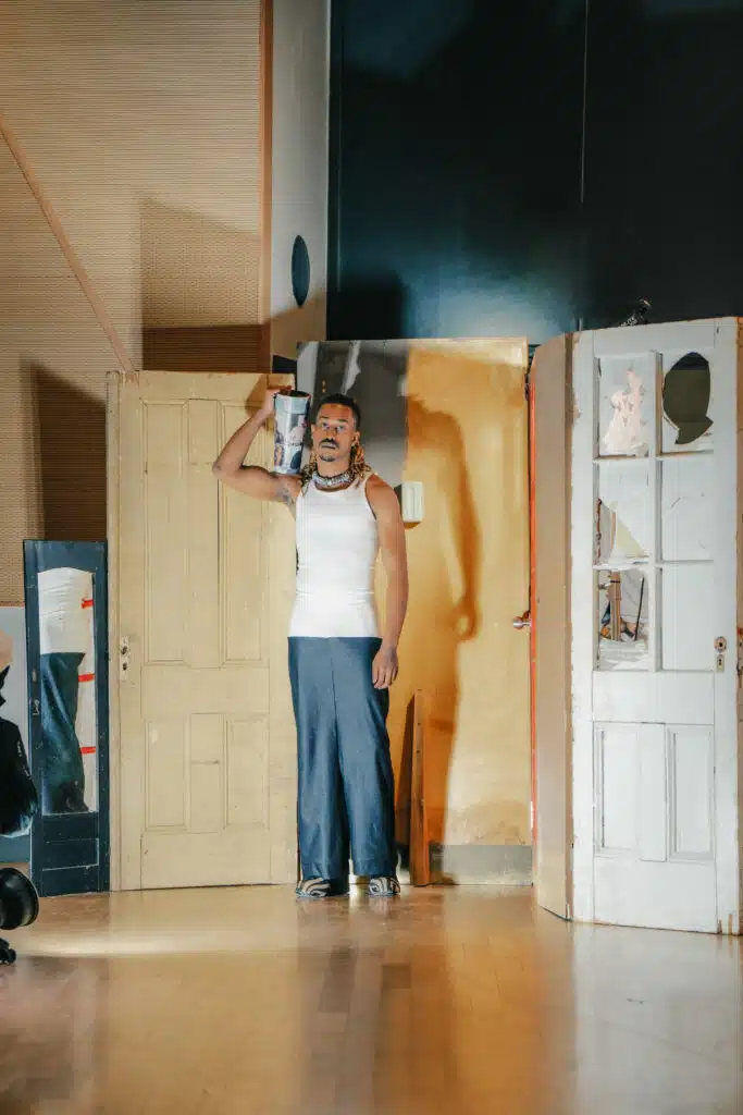 A man standing in front of a door and wearing a white shirt.