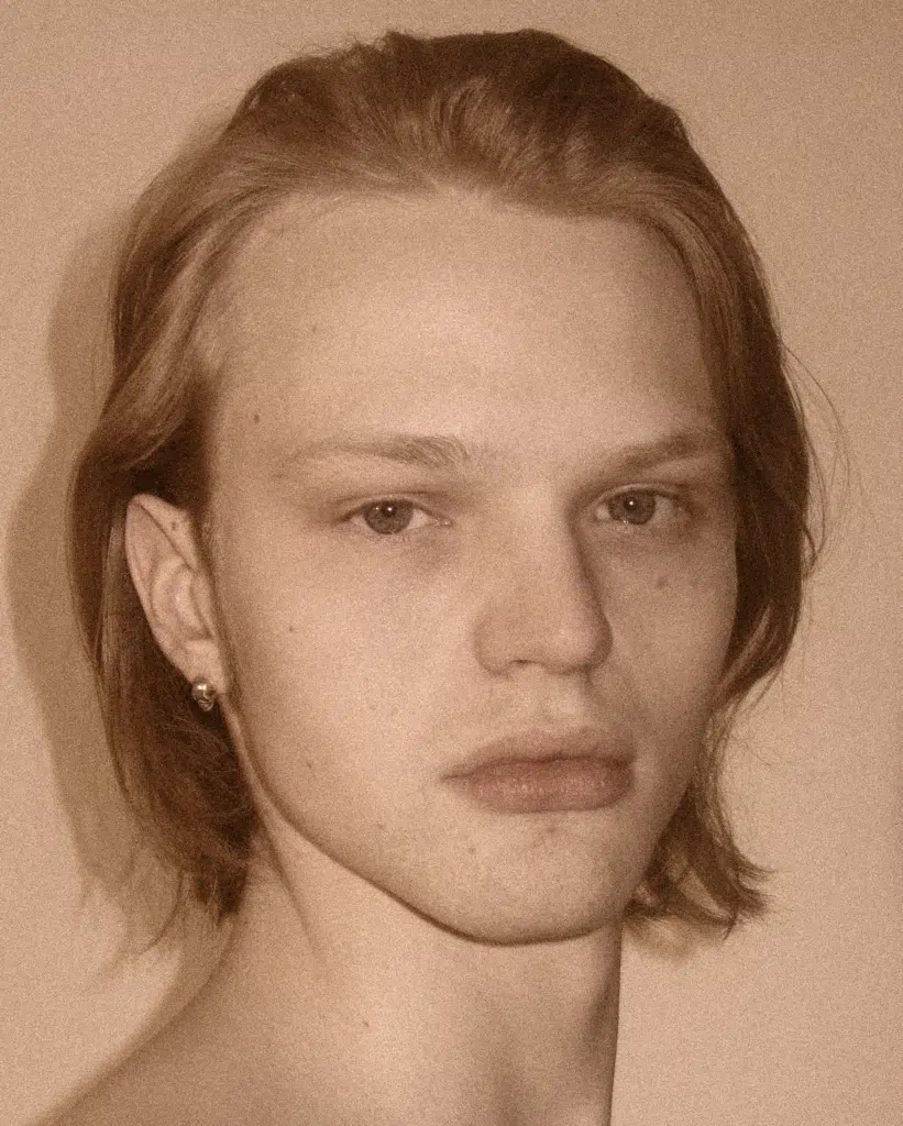 A young man with long hair and a piercing.