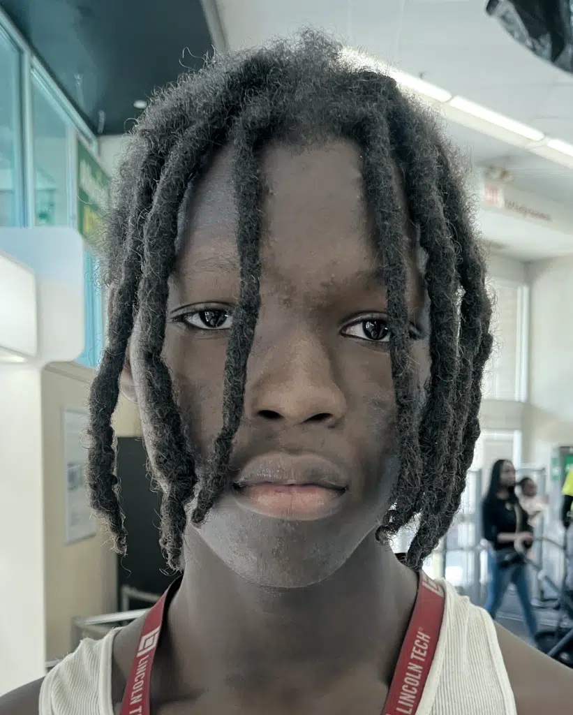 A young man with dreadlocks is looking at the camera.