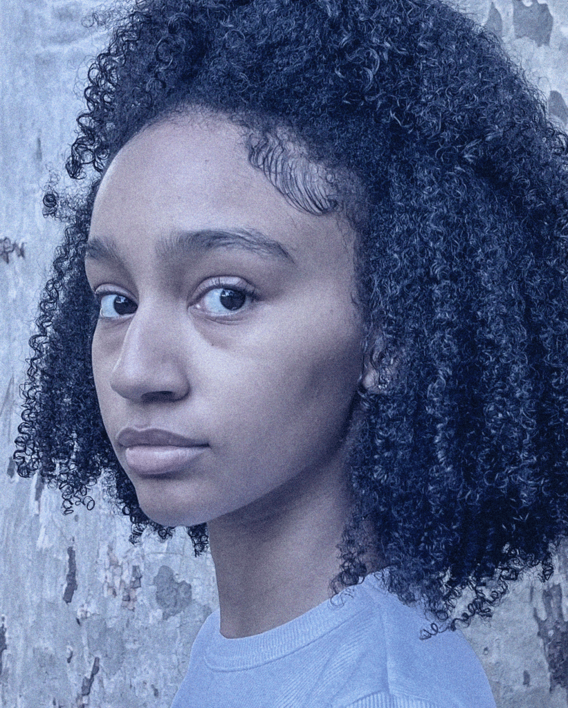 A young woman with curly hair is looking at the camera.