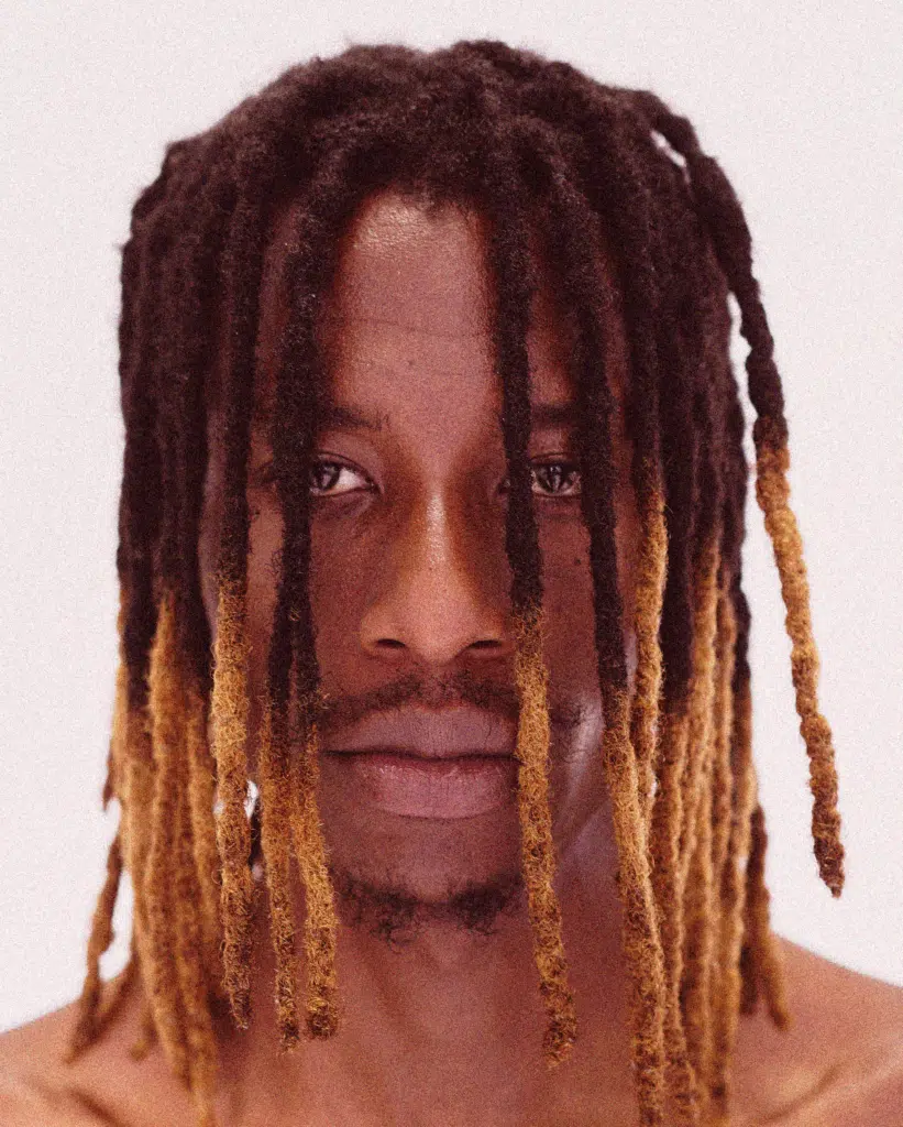 A man with dreadlocks is looking at the camera.