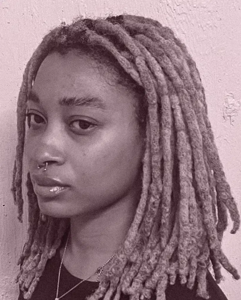 A young woman with dreadlocks is looking at the camera.