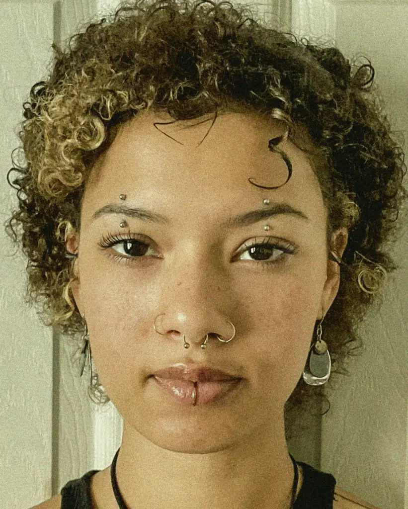 A woman with curly hair and a snake tattoo on her face.