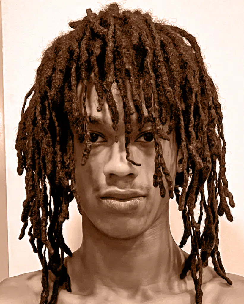 A man with dreadlocks is looking at the camera.