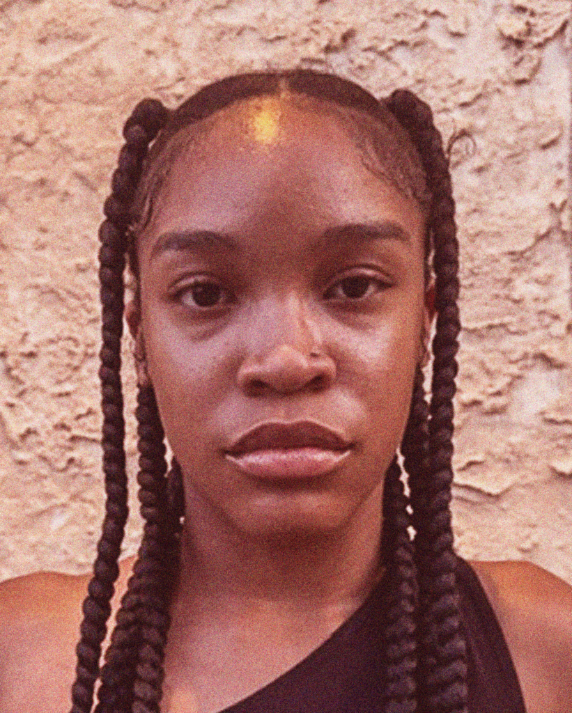 A woman with braids is standing in front of a wall.