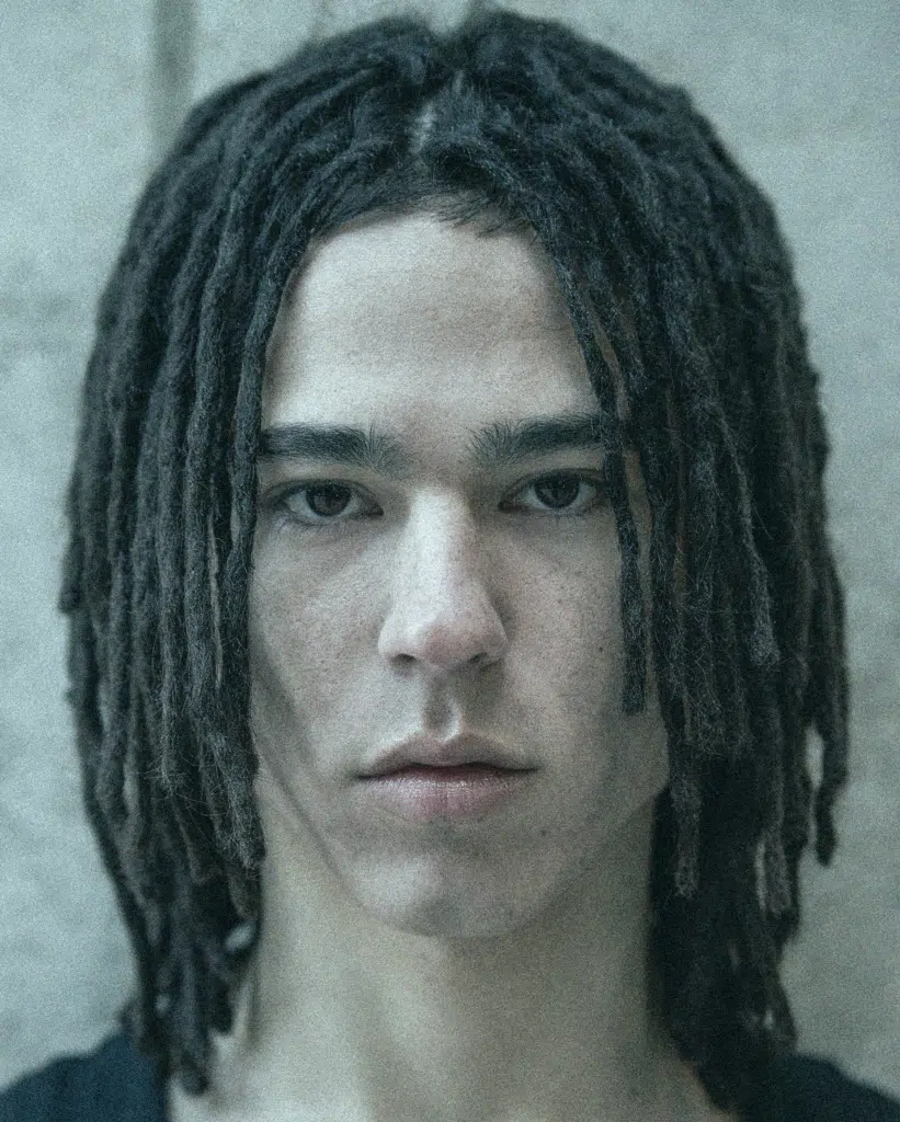 A man with dreadlocks is looking at the camera.