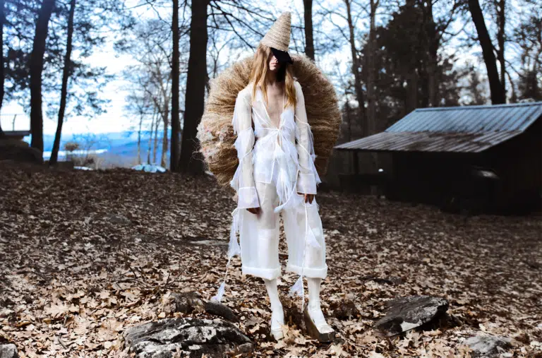 A woman in white dress and fur hat standing on leaves.