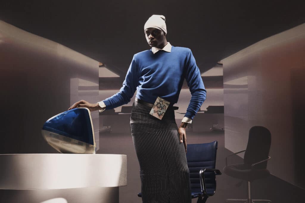 A man in blue shirt and black pants standing next to chair.