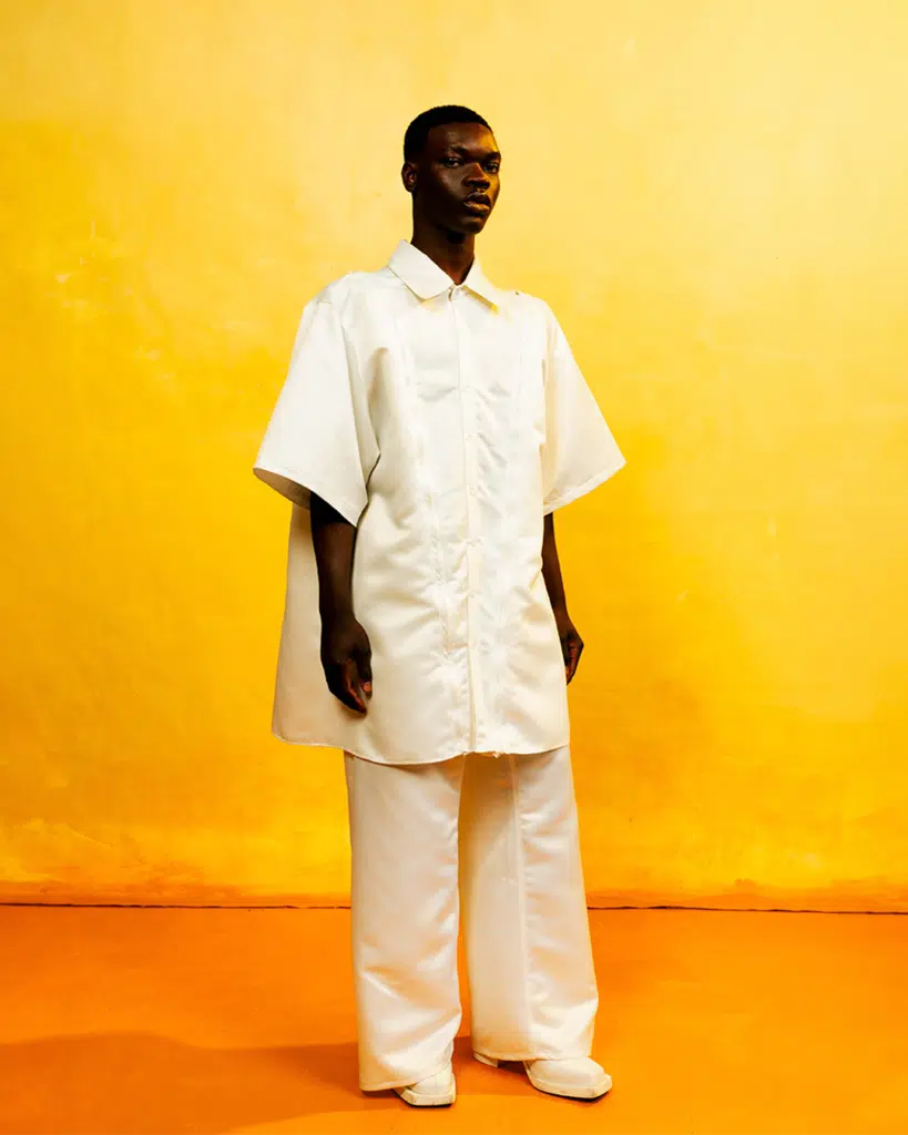 A man in white shirt and pants standing next to yellow wall.