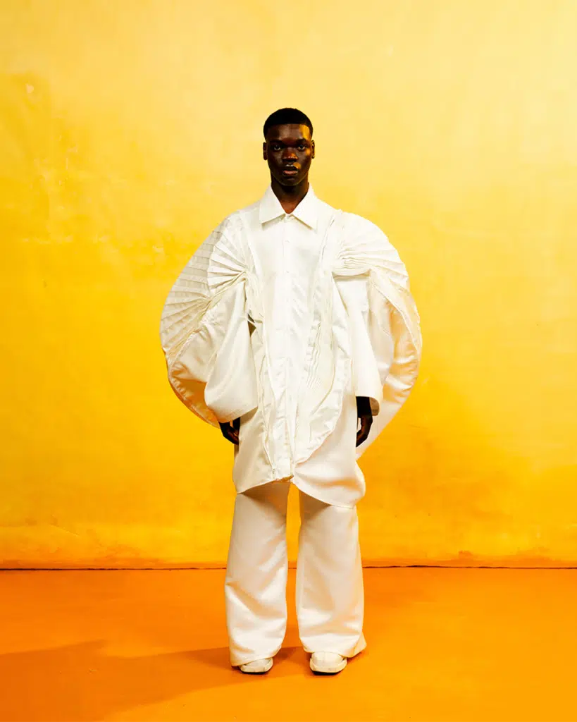 A man in white shirt and pants standing next to yellow wall.